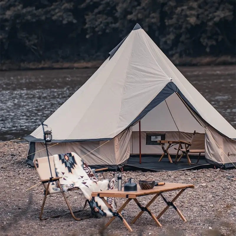 Beige outdoor camping tent by the river with seating area and table, perfect for camping trips.